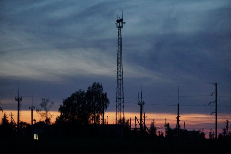 Silhouette of communication towers against a vibrant sunset sky with clouds.