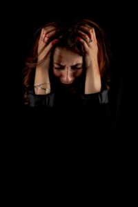 Woman holding head in distress against a dark background, symbolizing emotional struggle.
