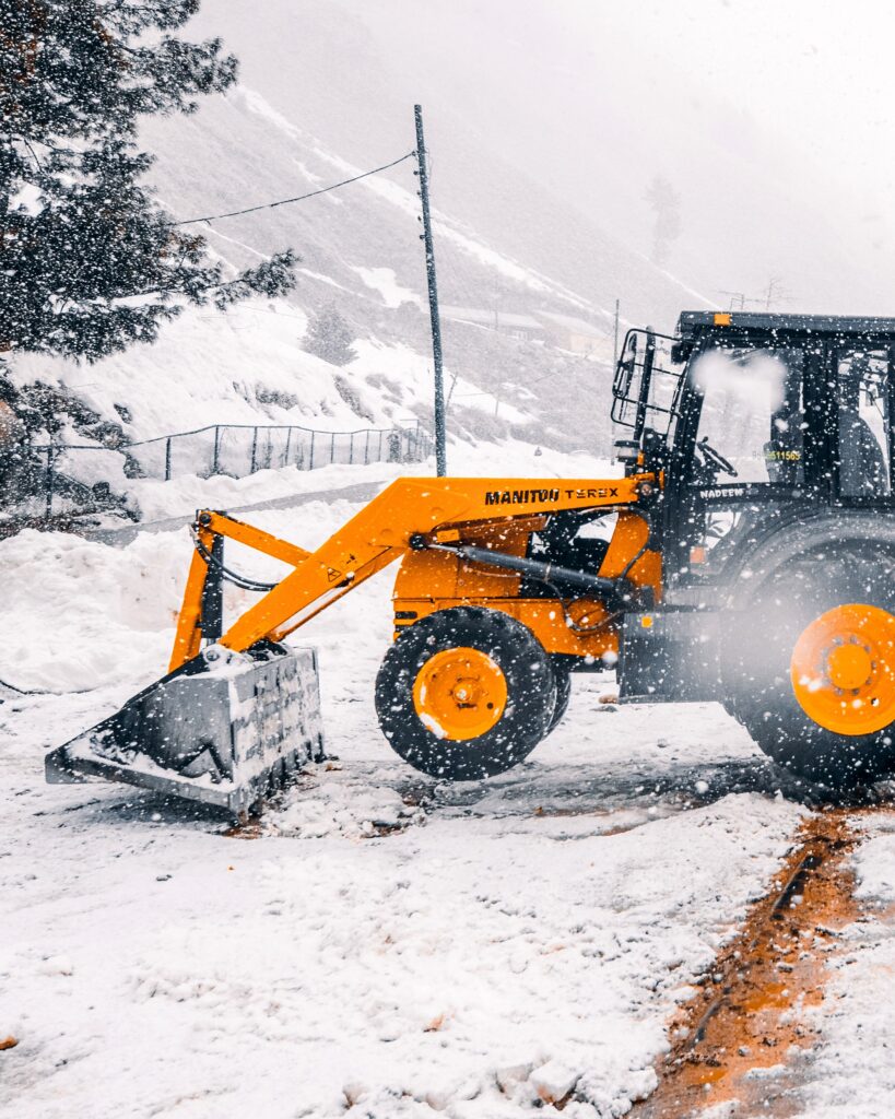 Yellow loader clearing snow on a winter day in a snowy landscape.